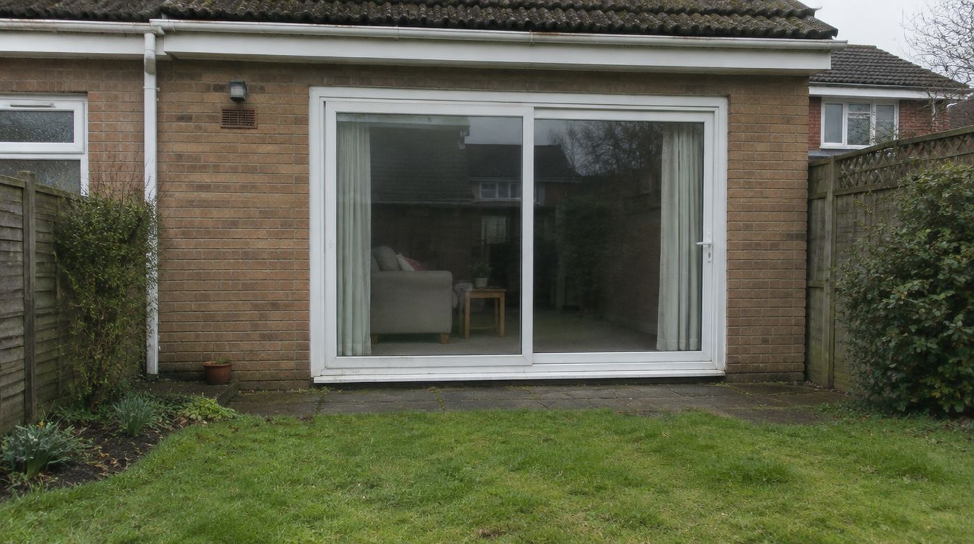 A dated 1990s uPVC sliding patio door on the back of a house, seen from the garden